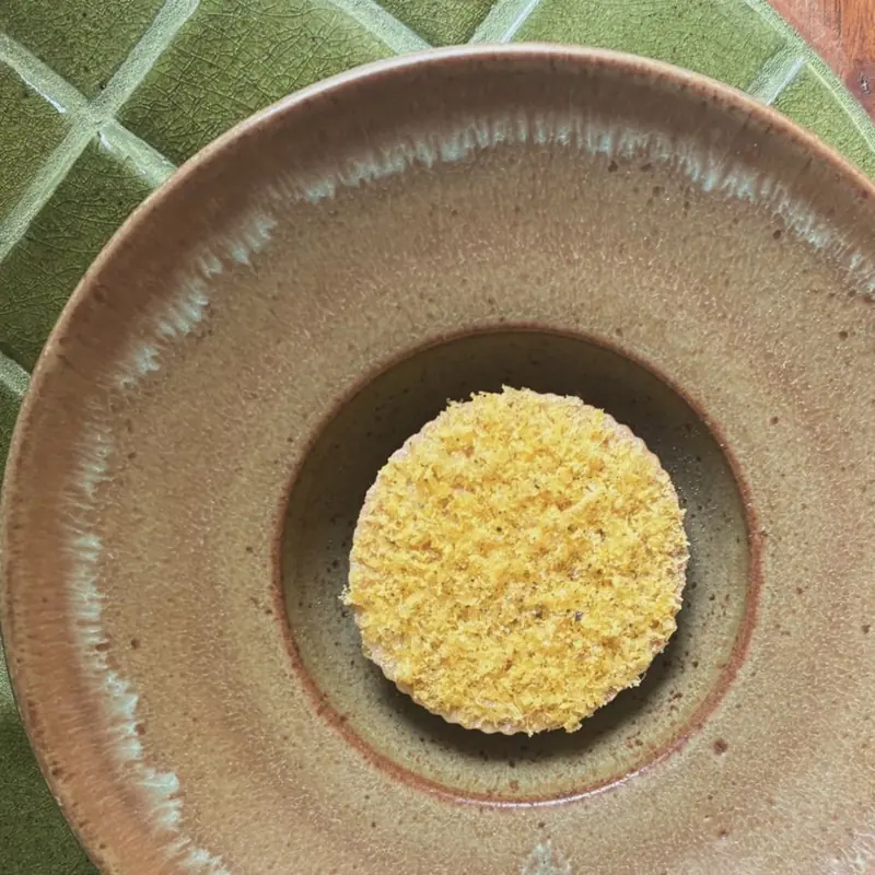A disc topped with grated egg yolk in a stoneware bowl