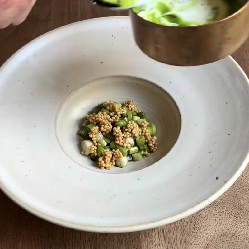 Green sauce poured over green vegetables and seeds in a white bowl