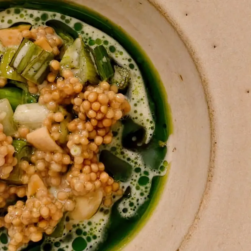 Close-up: golden seeds, green vegetables and herb oil in a foamy broth