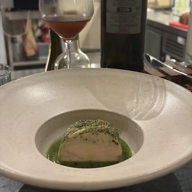 A herb-crusted white piece on a green sauce, with a glass of red wine