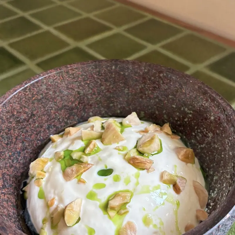 White mousse with almonds and green oil in a dark stoneware bowl
