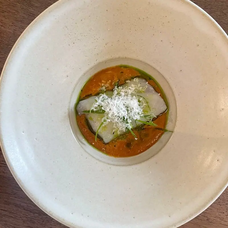 Thin slices in an orange sauce with herbs and a white grating, in a deep plate