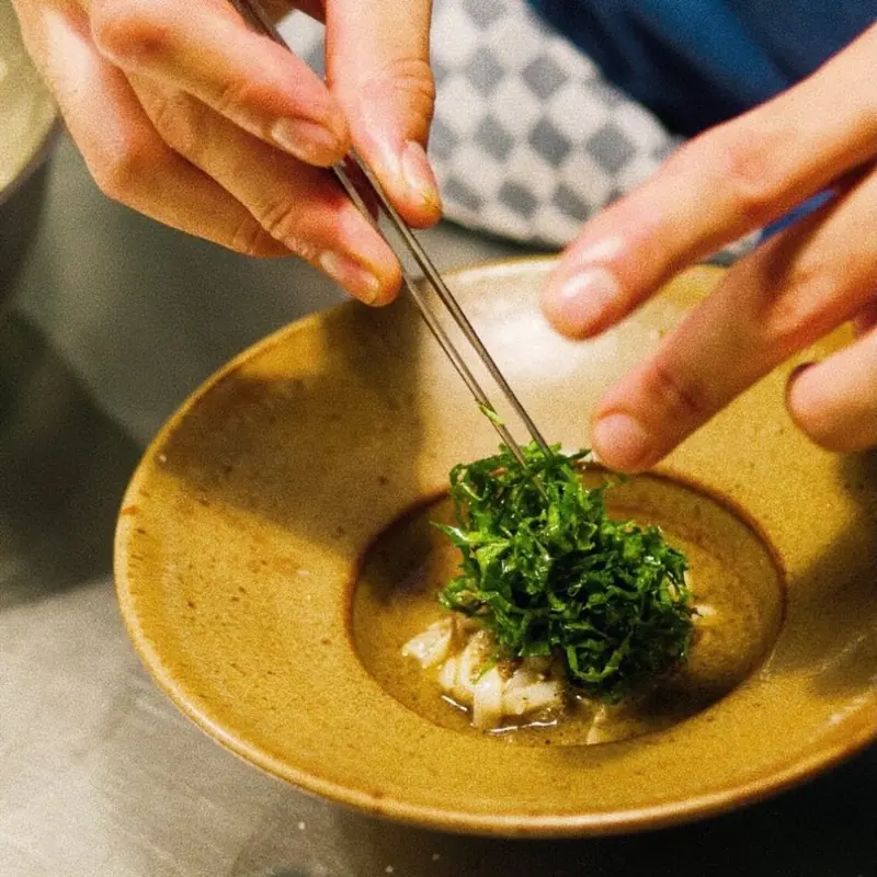 The chef placing chopped herbs with tweezers in the kitchen